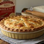 Freshly baked pie with a golden, flaky crust next to a bag of bread flour.