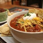 Bowl of thick taco soup with bitter cream, cheese, and tortilla chips.